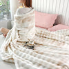 A fluffy cream colored gradient bubble fleece throw blanket draped over a bed with pink pillows.