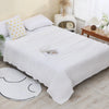 A white pure cotton muslin throw blanket is displayed on a bed with yellow accents and natural wood furniture.