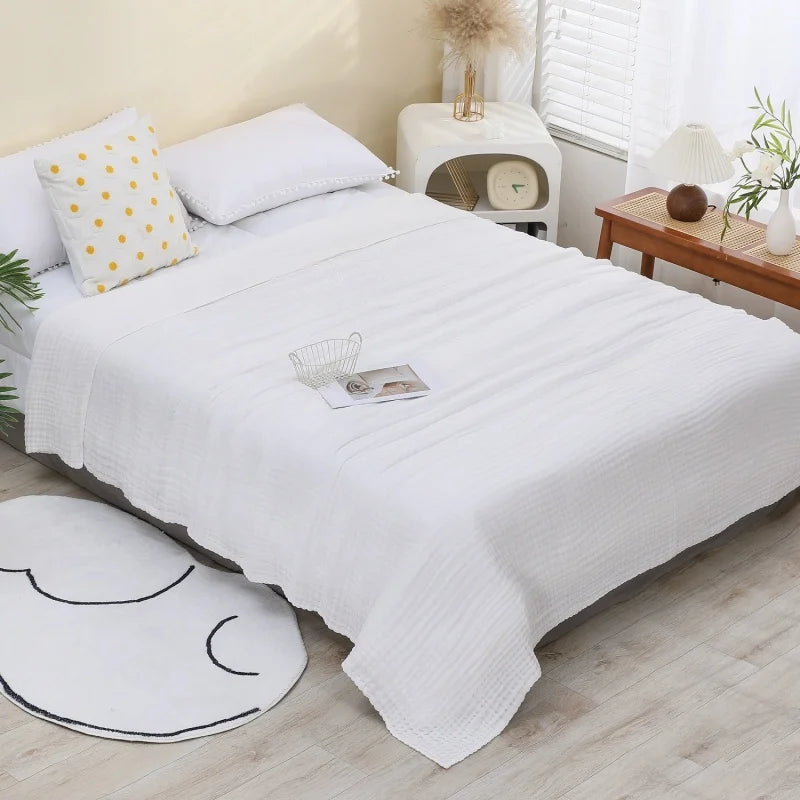 A white pure cotton muslin throw blanket is displayed on a bed with yellow accents and natural wood furniture.