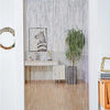 A white framed doorway decorated with a sheer silver tassel string curtain and a light wood console table.