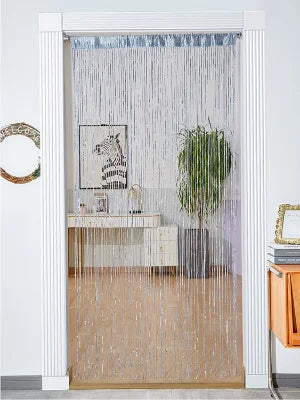 A white framed doorway decorated with a sheer silver tassel string curtain and a light wood console table.