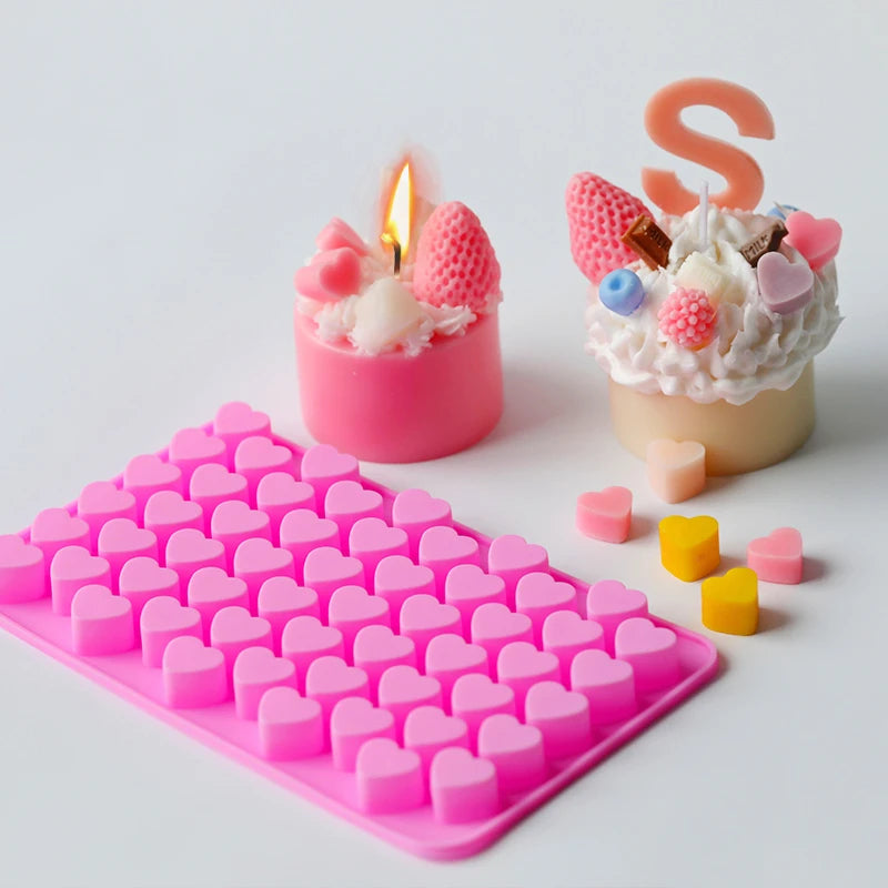 A pink silicone mold for making heart-shaped items, including candles, soap, and chocolate, is shown next to a lit candle.