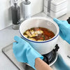 A hand wearing a blue scrubber-textured dishwashing glove is holding a white bowl of soup on a stovetop.