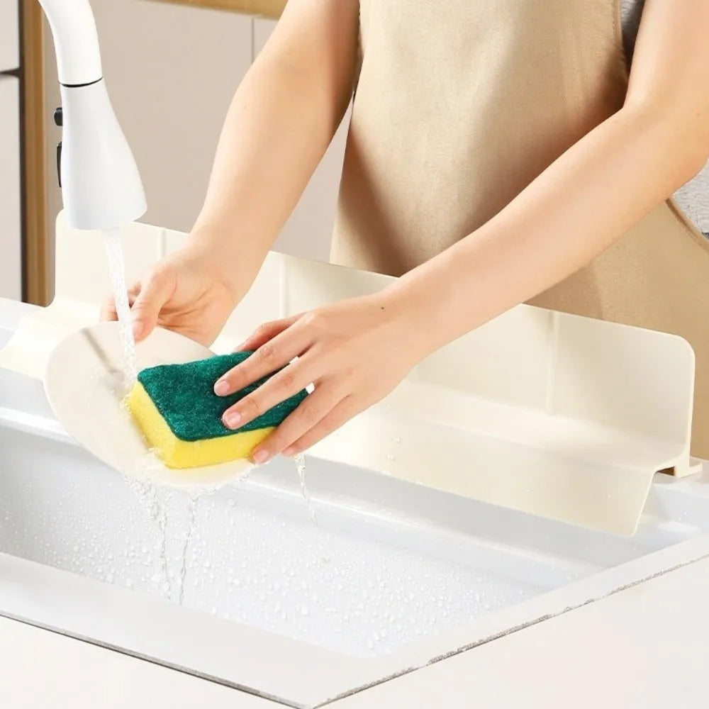 A hand is using a silicone sponge to clean a white sink with a water spray device.
