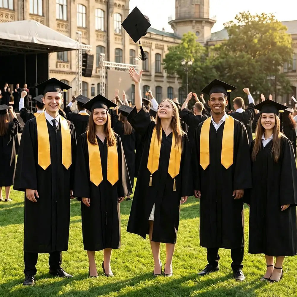 Five young adults in black graduation gowns and caps stand outdoors in a grassy field.