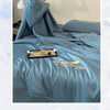 A teal ultra-soft cooling comforter is displayed on a bed, featuring embroidered text and a folded cover.
