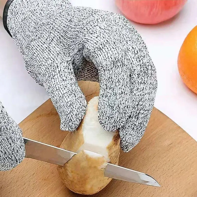 A hand wearing cut-resistant work gloves is shown cutting an orange on a wooden board.