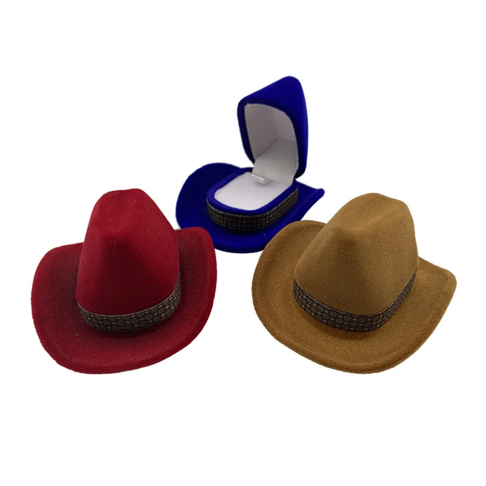 A maroon velvet cowboy hat is shown next to a tan felt cowboy hat and a blue jewelry storage box.