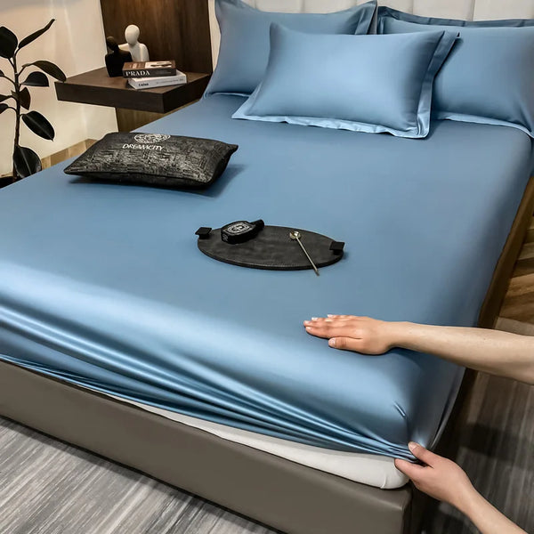 Juego de sábanas ajustadas de algodón liso azul claro de lujo con cojines a juego y un accesorio de cuero negro sobre la cama