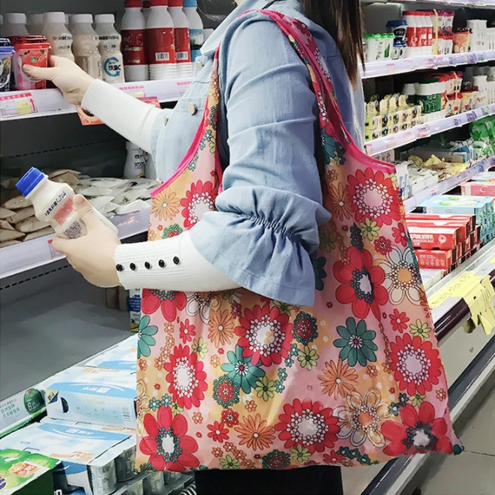 A person is holding a large pink floral reusable shopping tote bag while shopping in a store aisle.