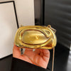 A hand holds a mini gold metal clutch bag with a gold chain strap against a dark background.