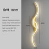 A vertical gold LED wall lamp with a curved design mounted on a wall.