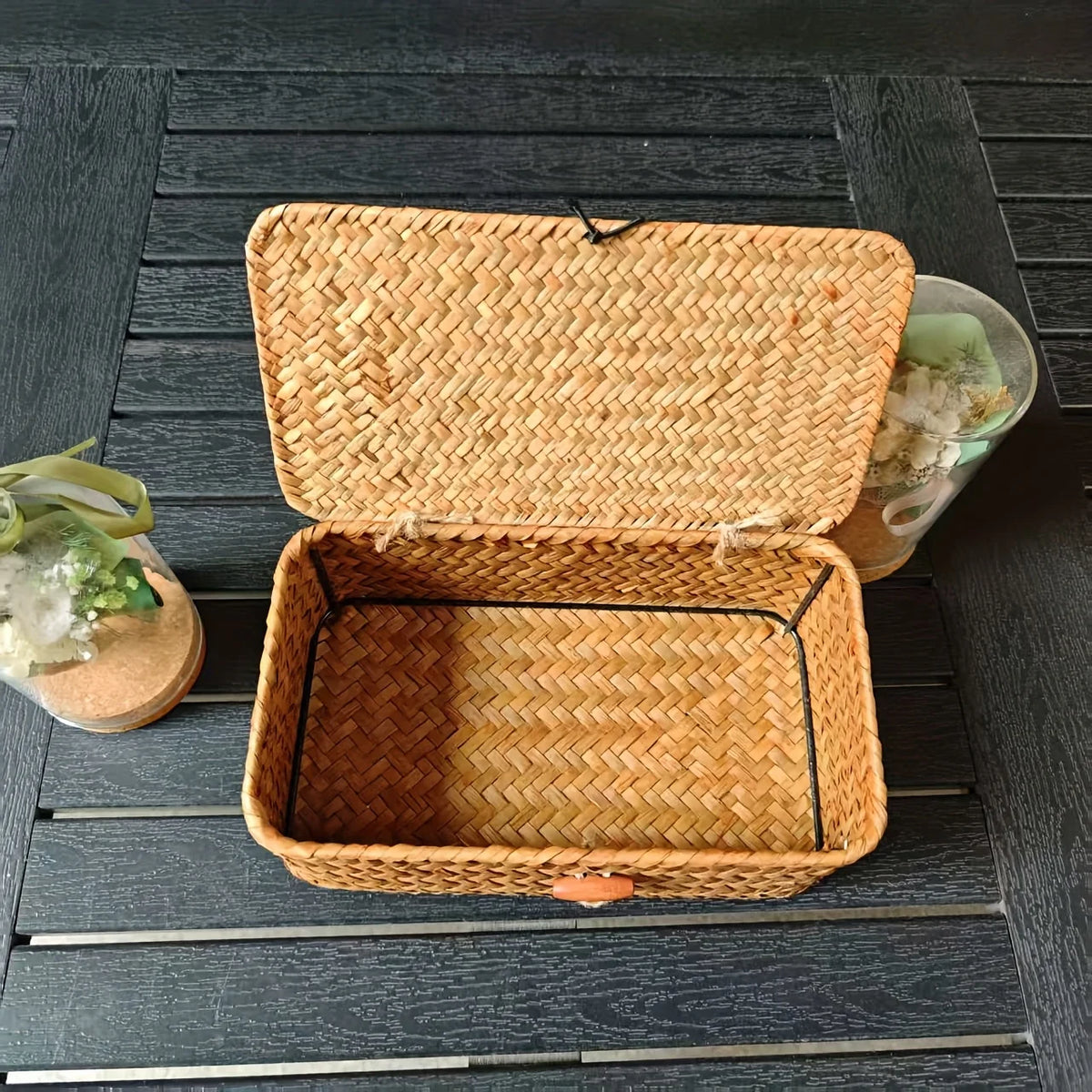 A woven rattan storage basket with a lid is shown open on a dark wooden surface.