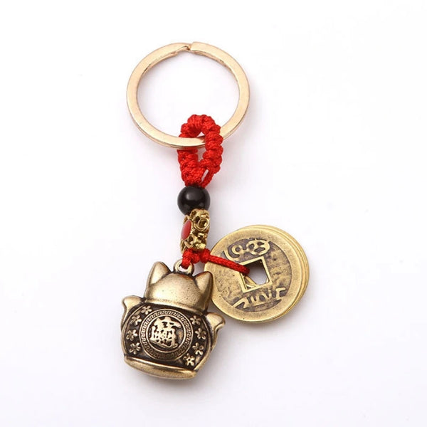 Vintage lucky cat keychain featuring a coin design with five emperors and a red tassel.