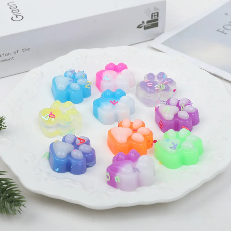 A collection of colorful squishy cat paw fidget toys in various shades of blue, pink, and green arranged on a white plate.