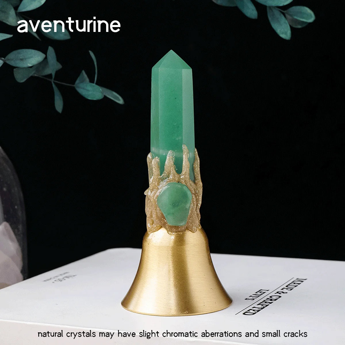 A natural green aventurine crystal point set in a brass bell on a white surface.