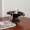 A black ceramic soap dish with an elevated stand holding a white angel figurine on a wooden table.