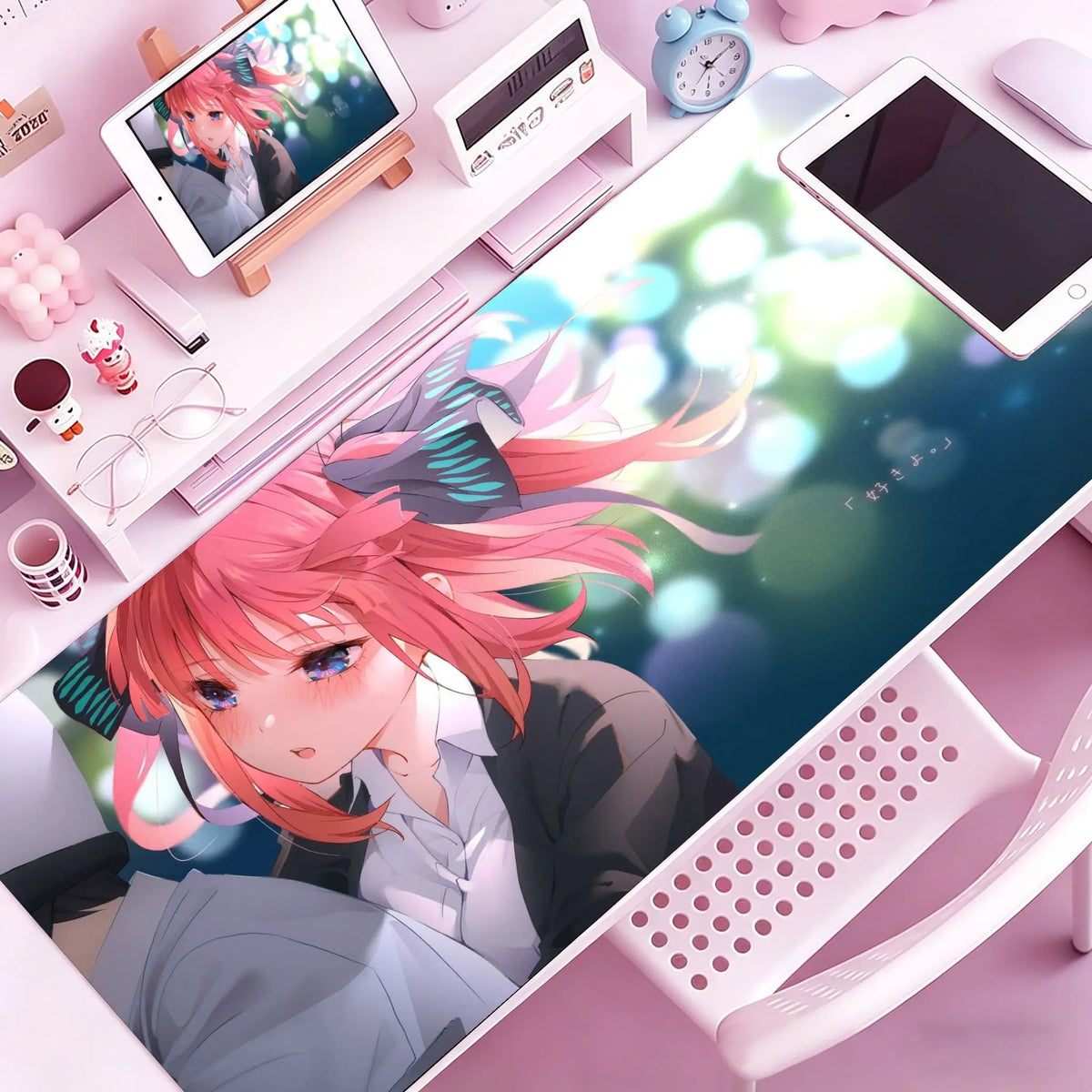 Anime character illustration on a pink mouse pad desk mat with surrounding stationery and a tablet.