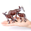 Three realistic brown animal figurines, resembling gazelles or antelopes, are held in a person's hand.