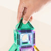 A hand is assembling a colorful magnetic building tile structure made of green, blue, and purple pieces.