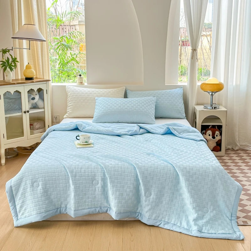 A light blue waffle-weave summer quilt is displayed on a bed in a bright, airy bedroom.