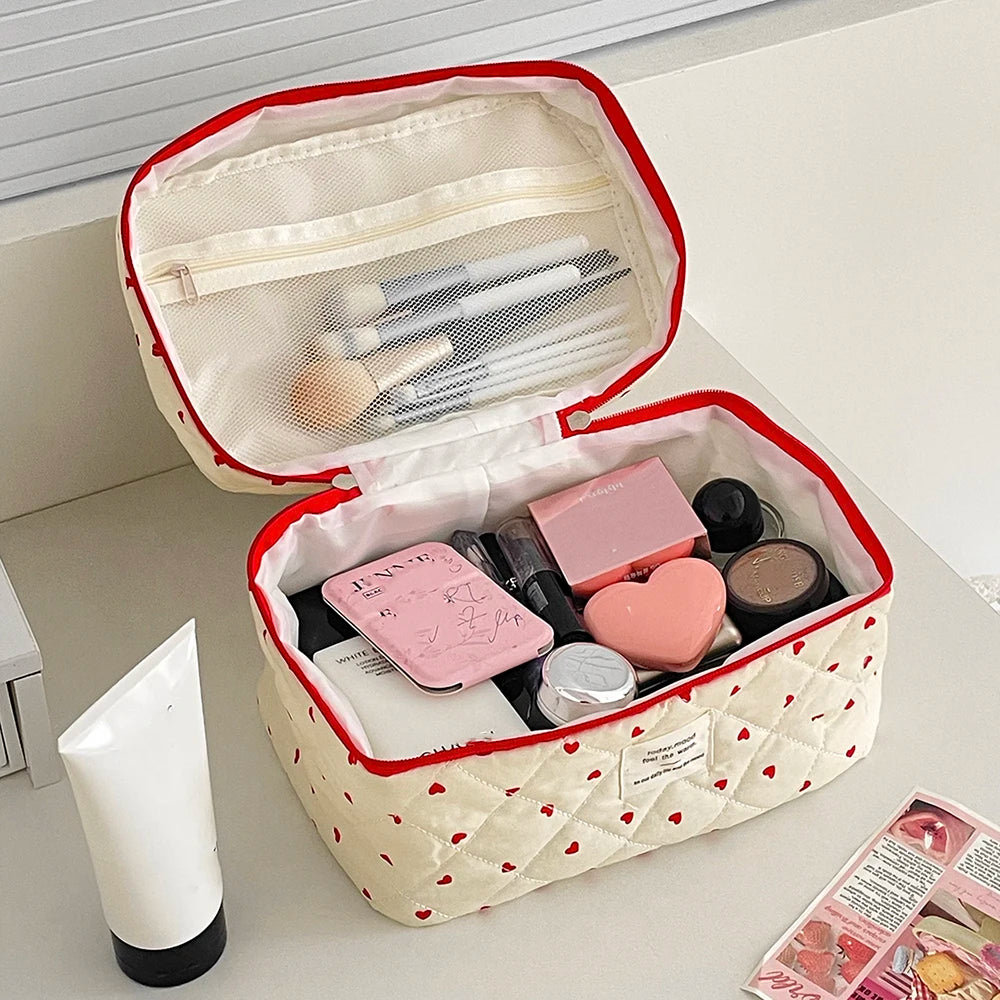 A quilted pink makeup bag with a large zipper closure is open, revealing various cosmetic products inside.