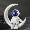 A white astronaut figurine with a blue helmet and stars, sitting on a curved silver base.