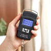 A hand holds a black portable digital luggage scale with an LCD display showing 0.000 kg.
