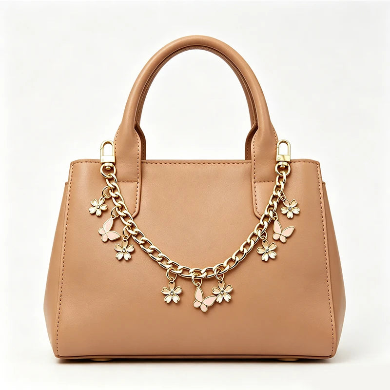 A tan leather handbag with a top handle and decorative gold chain featuring small flower charms.