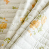 A close-up of a white floral quilted bedspread with orange and green accents.