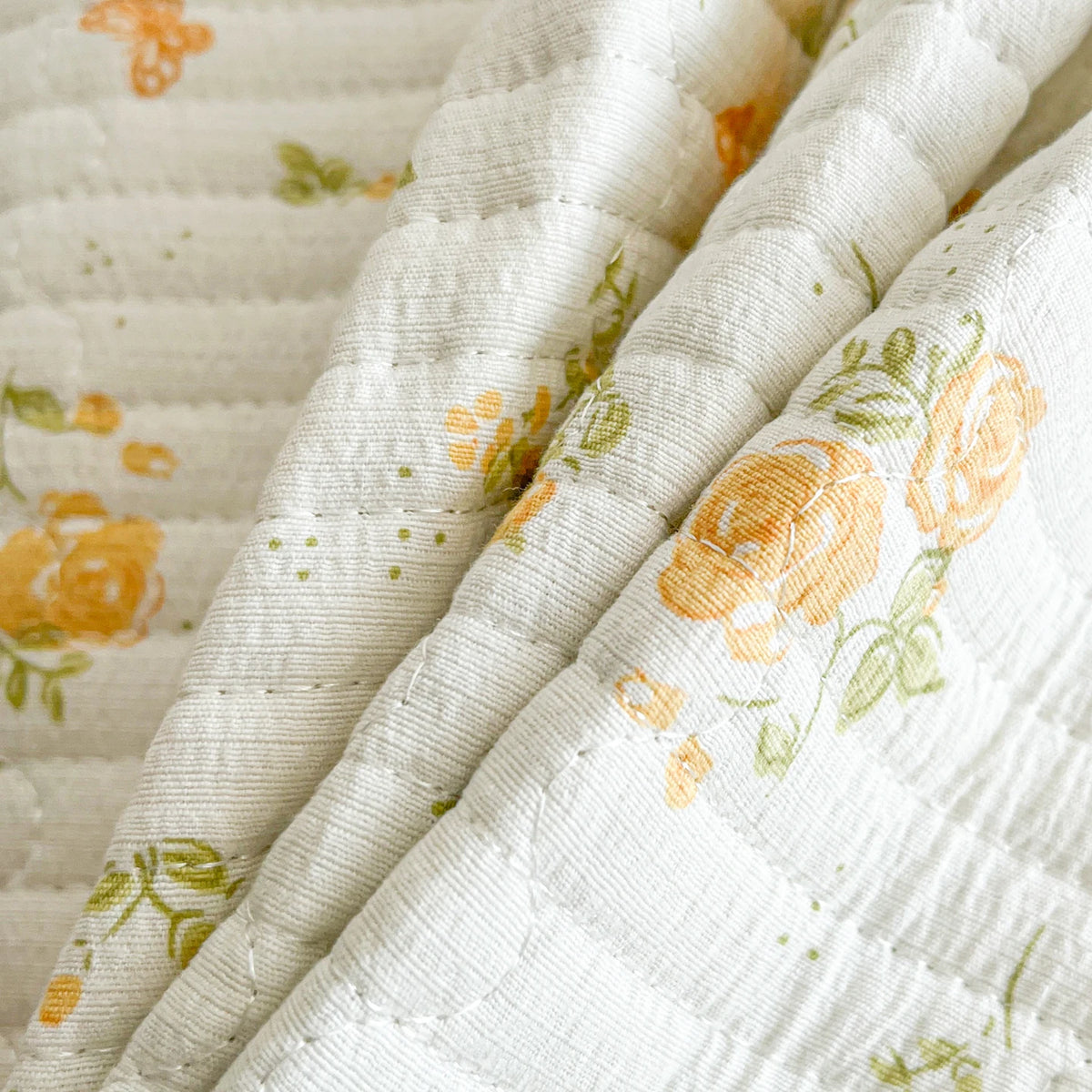 A close-up of a white floral quilted bedspread with orange and green accents.