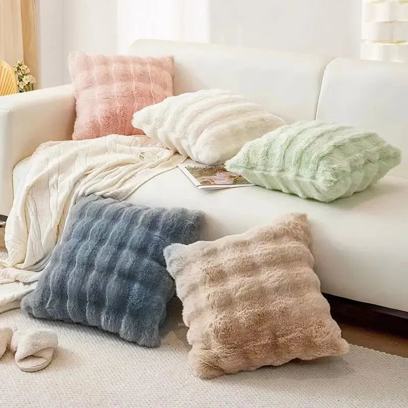 A collection of fluffy decorative pillows in shades of pink, beige, and green resting on a white sofa.