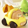 A yellow push-and-go toy car shaped like a brown bear, being held by a white hand next to a green tree.