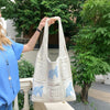 A person holds up a white handwoven knit tote bag with a hollow design outdoors.