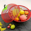 A red metal fruit basket with a mesh cover filled with various fruits like apples, lemons, and oranges.