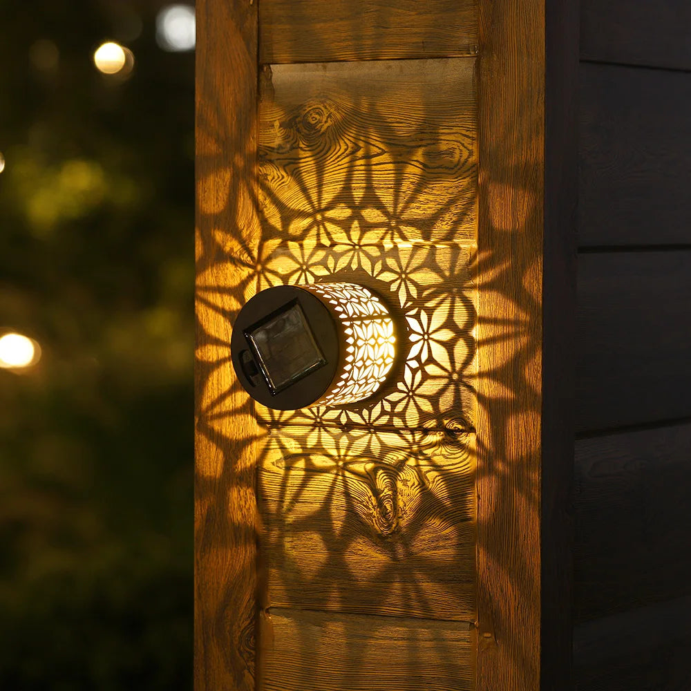 Una luz de pared solar con patrón mandala proyecta sombras florales sobre el panel de madera.