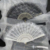 A vintage lace folding hand fan in black and white is displayed on sheer fabric.