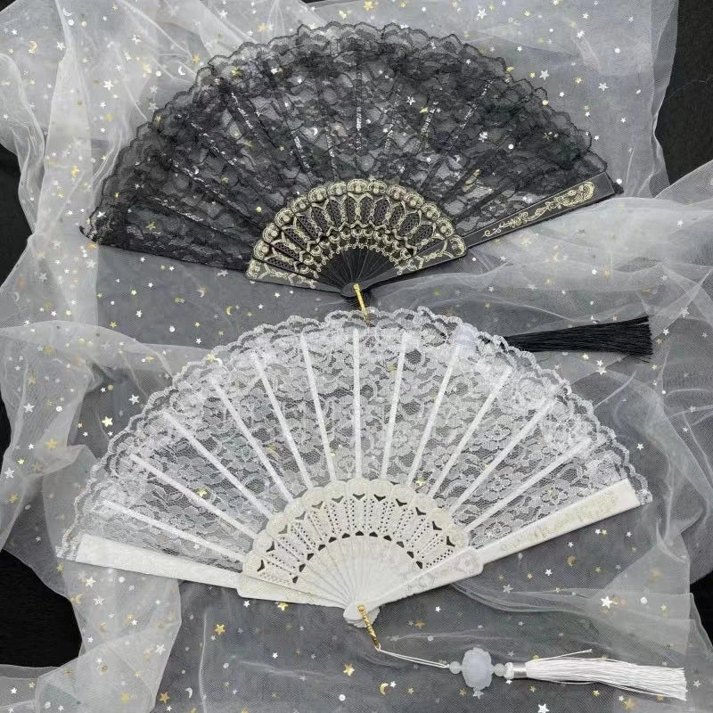 A vintage lace folding hand fan in black and white is displayed on sheer fabric.