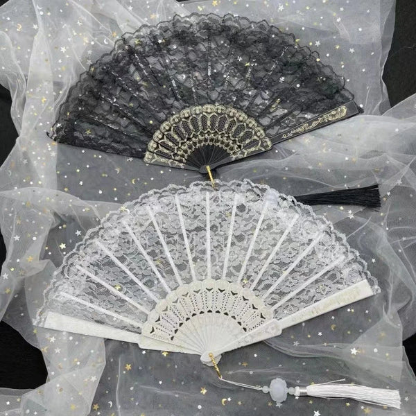 A vintage lace folding hand fan in black and white is displayed on sheer fabric.