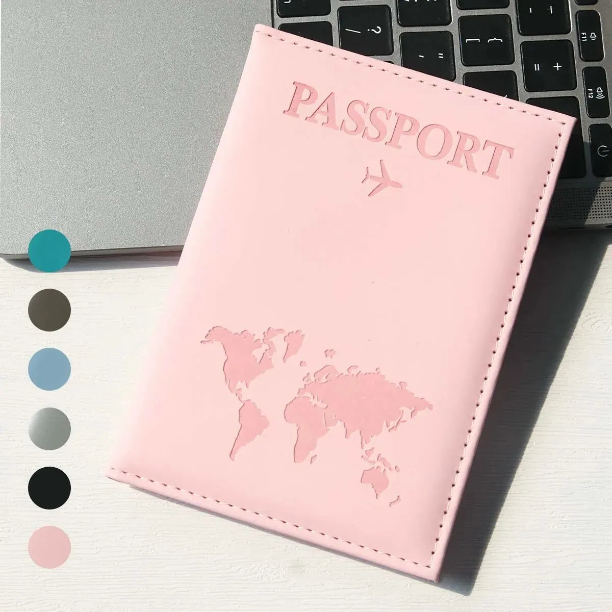 Pinkes schlankes Kunstleder-Reisepass-Cover mit erhabenem Weltkarten-Design neben einer Laptop-Tastatur.