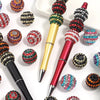 A set of five resin rhinestone beads with a two-tone striped design are displayed alongside a gold and red pen.
