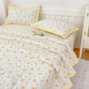 White quilted bedspread with orange floral pattern and yellow trim, featuring matching pillows.