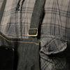 Close-up of a dark gray plaid denim and waxed canvas work apron with a brass buckle and pocket.