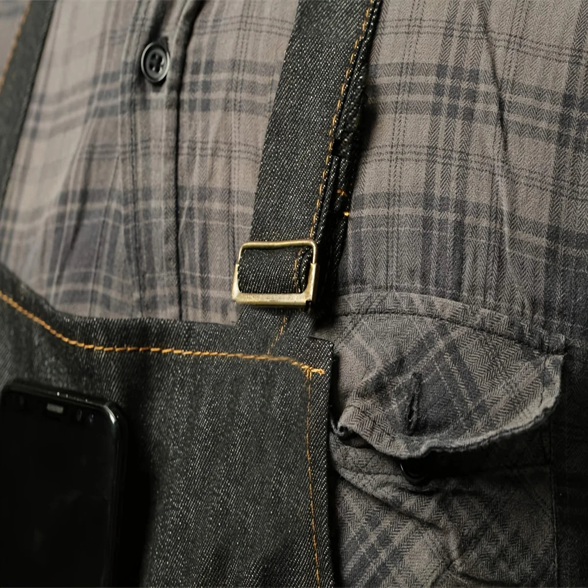 Close-up of a dark gray plaid denim and waxed canvas work apron with a brass buckle and pocket.