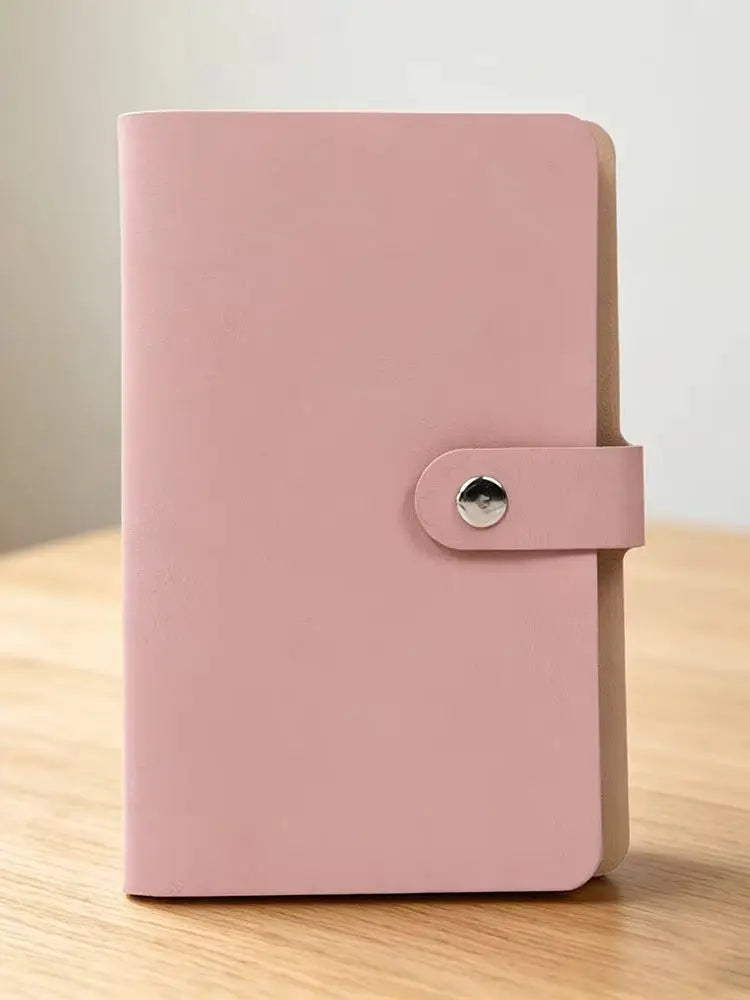 A pink leather organizer binder with a snap closure is shown on a wooden surface.