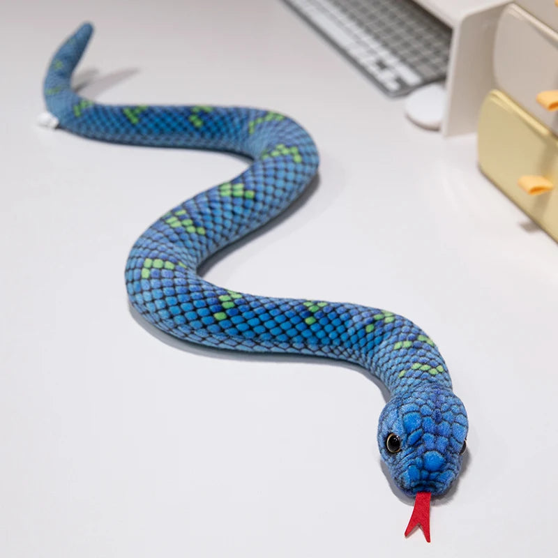 A blue and green lifelike snake plush toy with a red tip is coiled on a white surface.