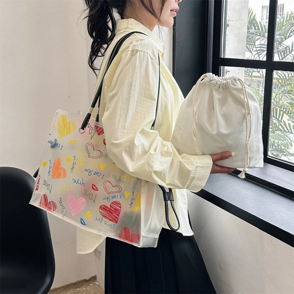 A person holds a white canvas tote bag and a matching transparent tote bag with an inner pouch next to a window.