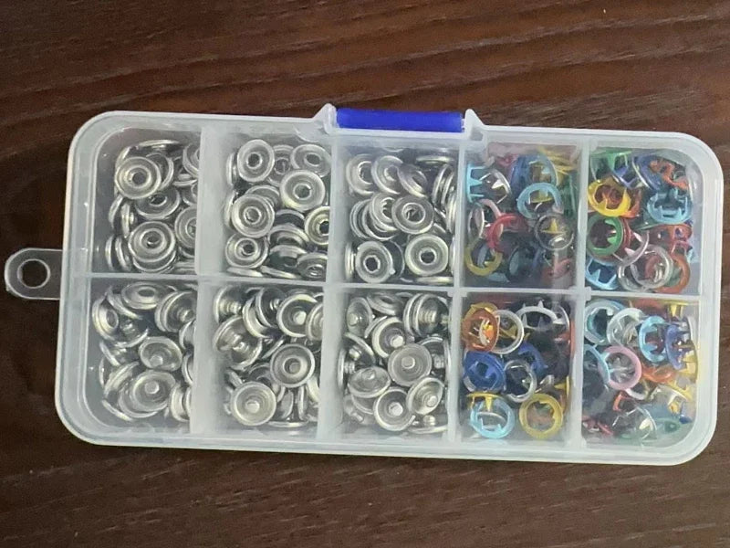 Una caja de plástico transparente contiene diversas pinzas y aros metálicos en múltiples compartimentos.