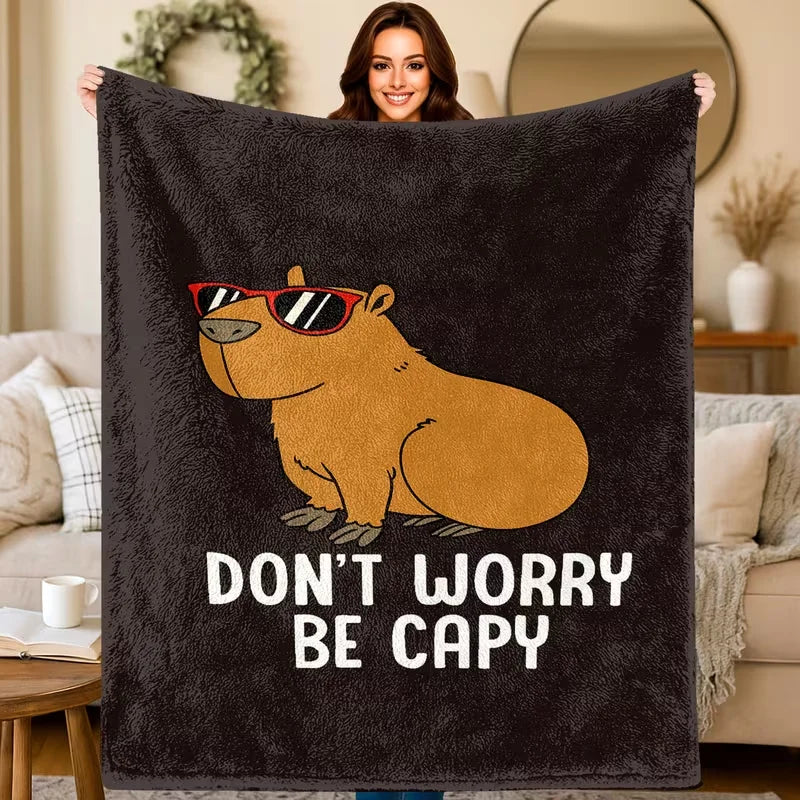 A dark gray flannel throw blanket featuring a cartoon illustration of a smiling capybara with sunglasses.