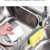 A hand is placing a white sponge into a stainless steel holder on a kitchen sink.